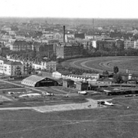 Lotnisko Mokotów. Dobrze widoczne trzy hangary i inne budynki. Centralnie widoczny budynek to dworzec. Poniżej utwardzona centralna płyta postojowa i pole wzlotów. Nieco na prawo widoczny na bocznicy kolejowej pociąg, którym dostarczono między innymi części zamienne i paliwo.